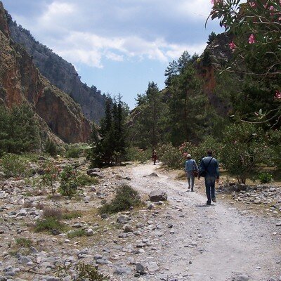 Hikers strolling along a rugged trail surrounded by lush greenery and dramatic mountain cliffs in Crete’s scenic landscape.