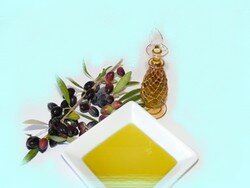 Dish of golden olive oil beside a glass bottle and a sprig of black olives