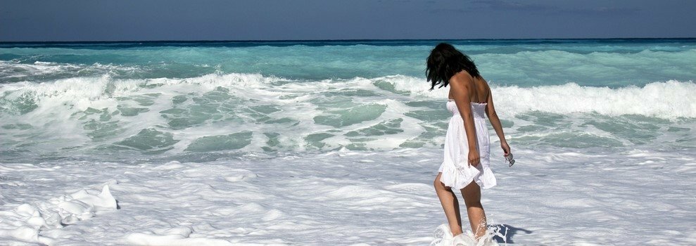 Woman in a white dress paddling in the surf on a Crete beach